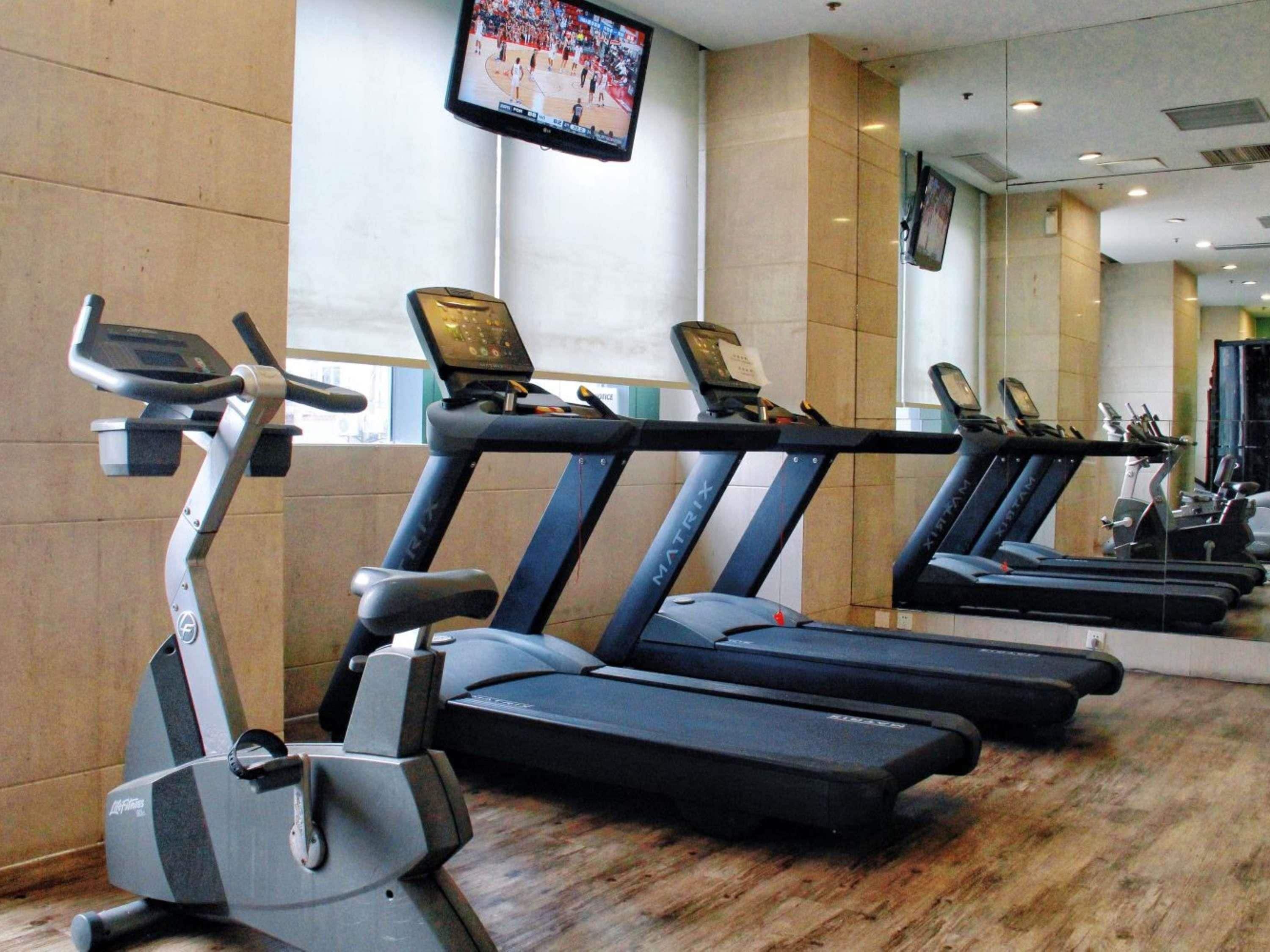 A gym with treadmills, an elliptical, and a television screen displaying a sports event.