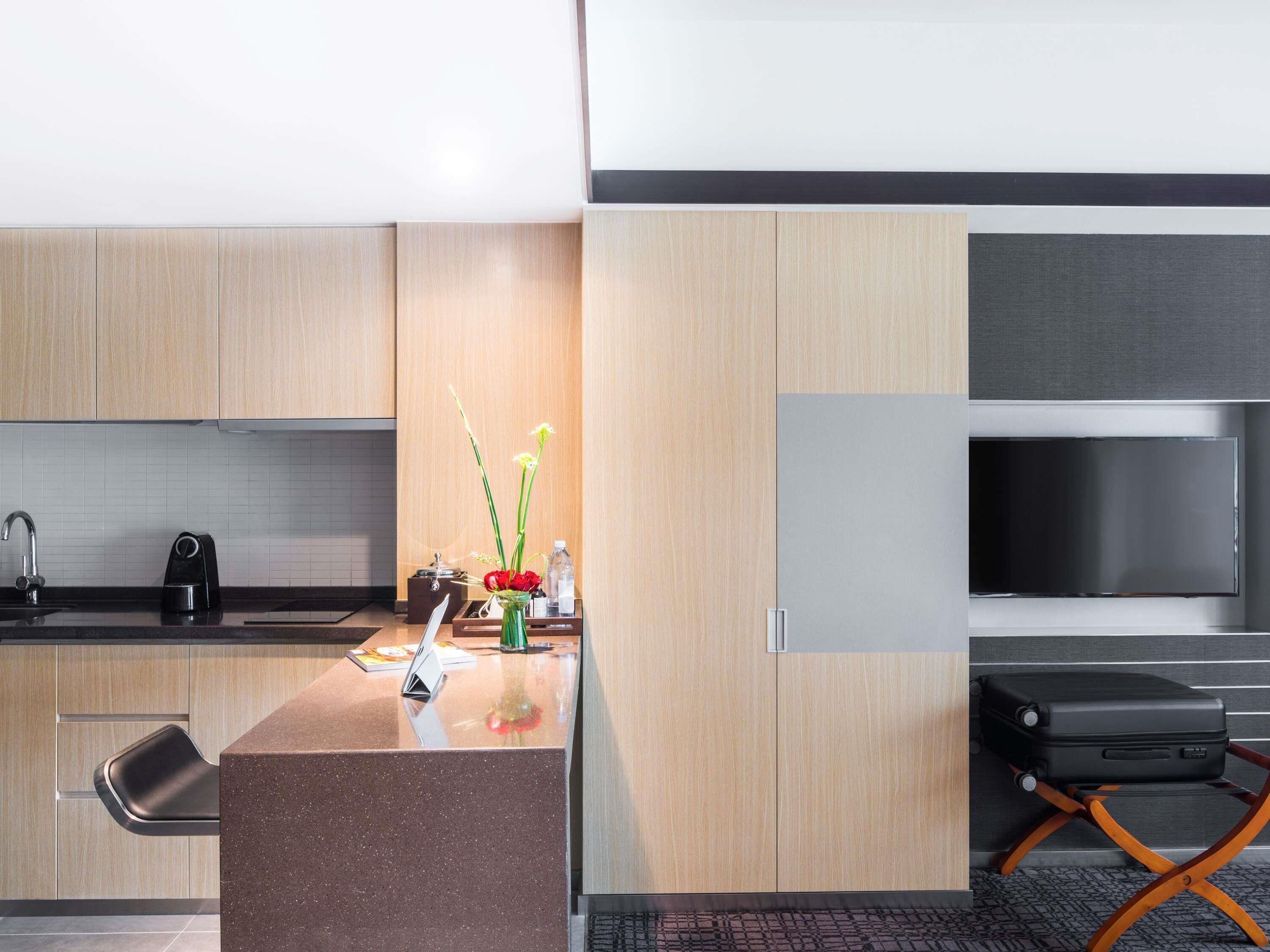 A modern kitchen with wooden cabinets, a granite countertop, a built-in stove, and a flat-screen TV.