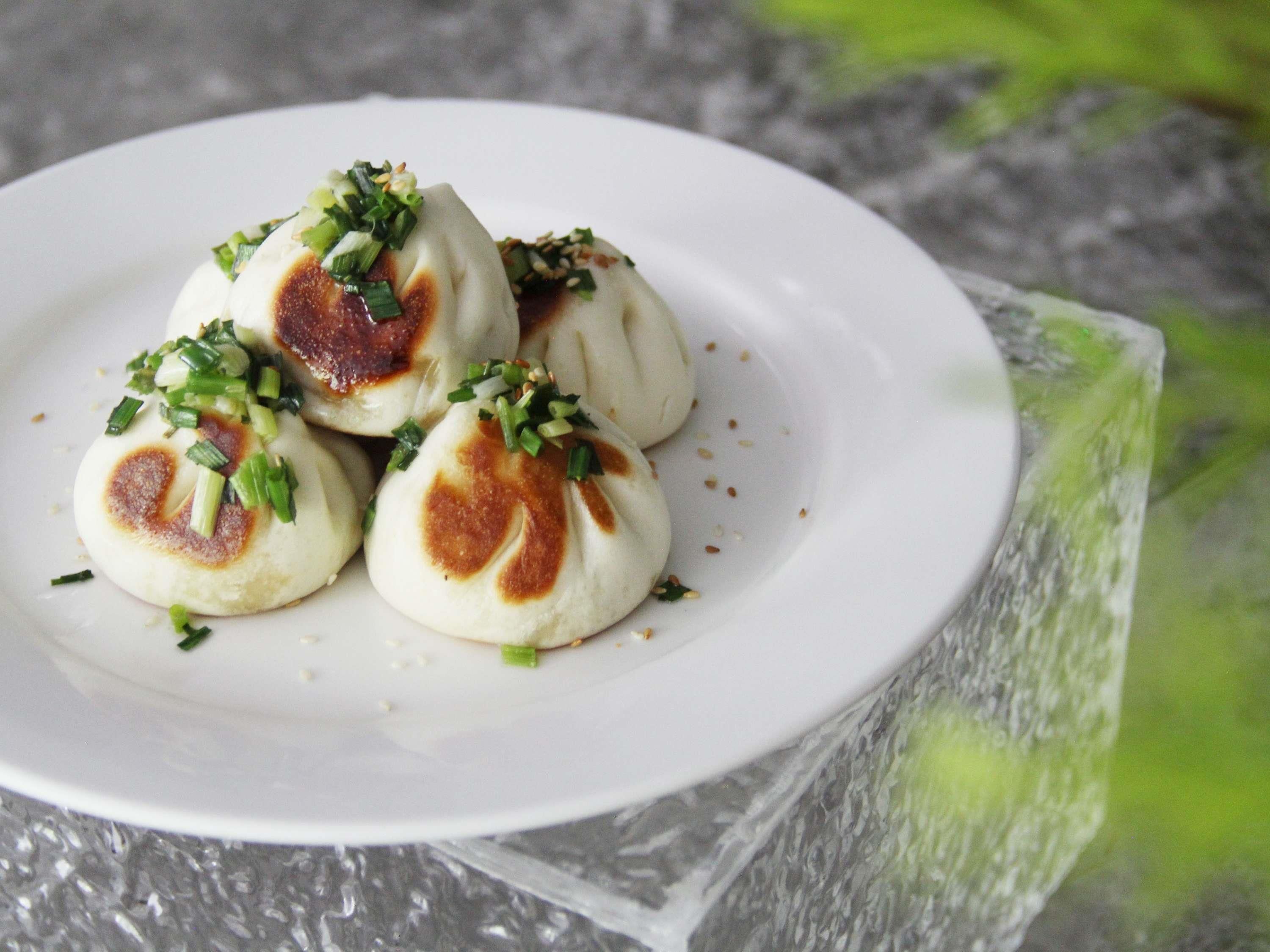 A plate of steamed buns garnished with green onions and sesame seeds.