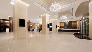 A spacious lobby with a reception desk, chandeliers, and a modern design.