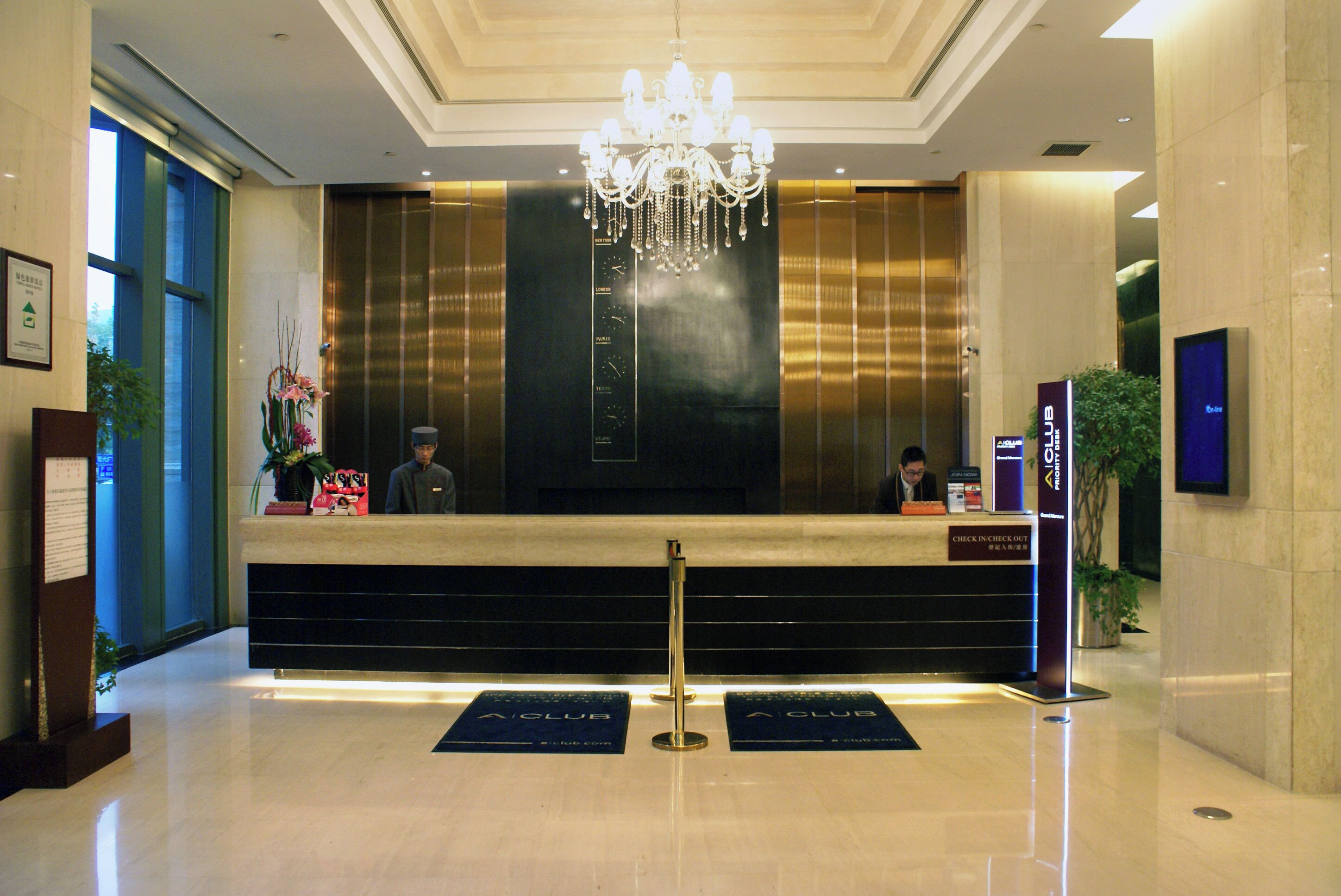 A hotel reception desk with a chandelier, a digital screen, and a sign for the A Club.