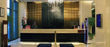 A hotel reception desk with a chandelier, a digital screen, and a sign for the A Club.