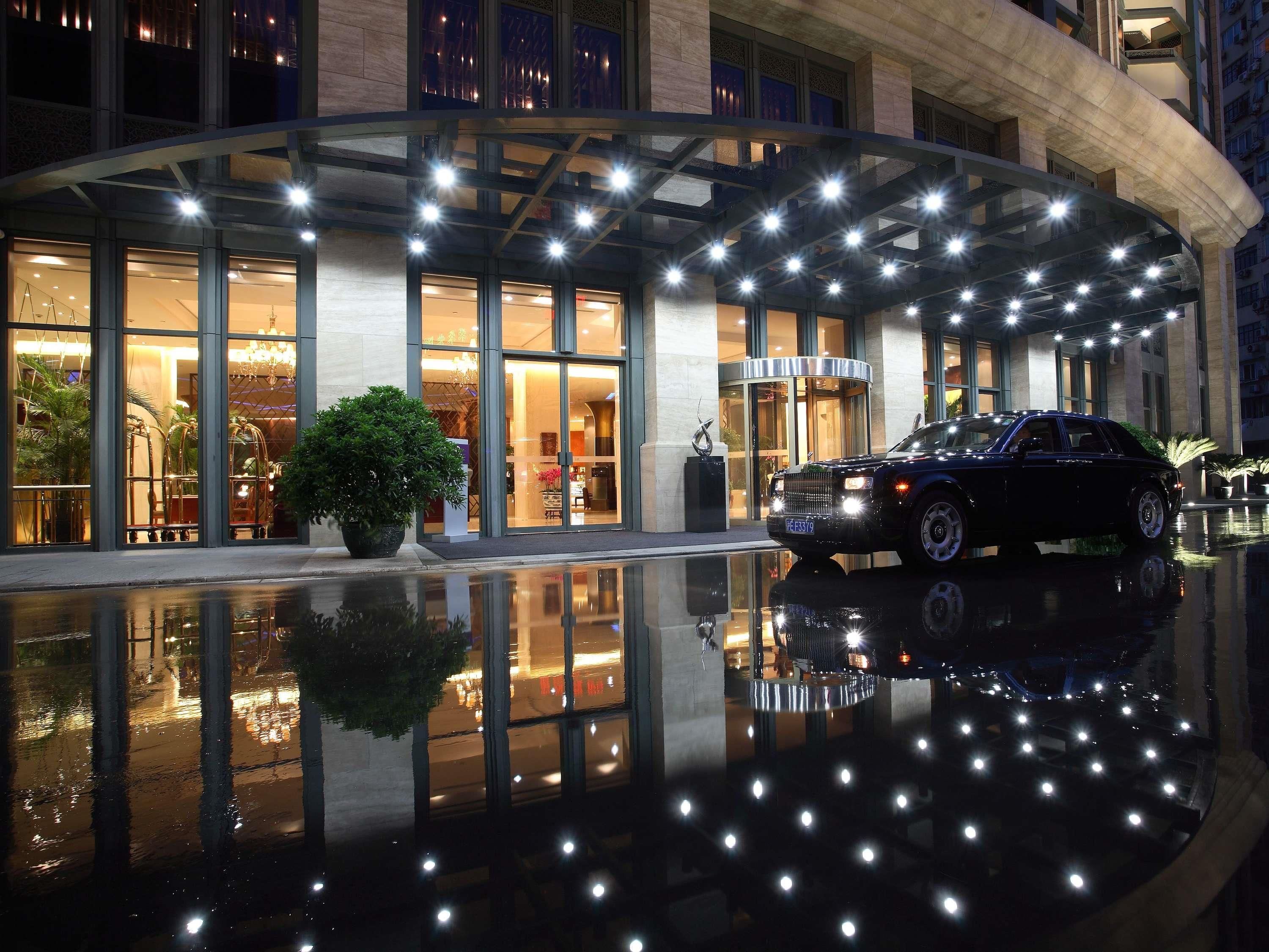 A modern hotel with a reflective pool, large glass windows, and a black car parked in front.