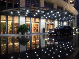A modern hotel with a reflective pool, large glass windows, and a black car parked in front.
