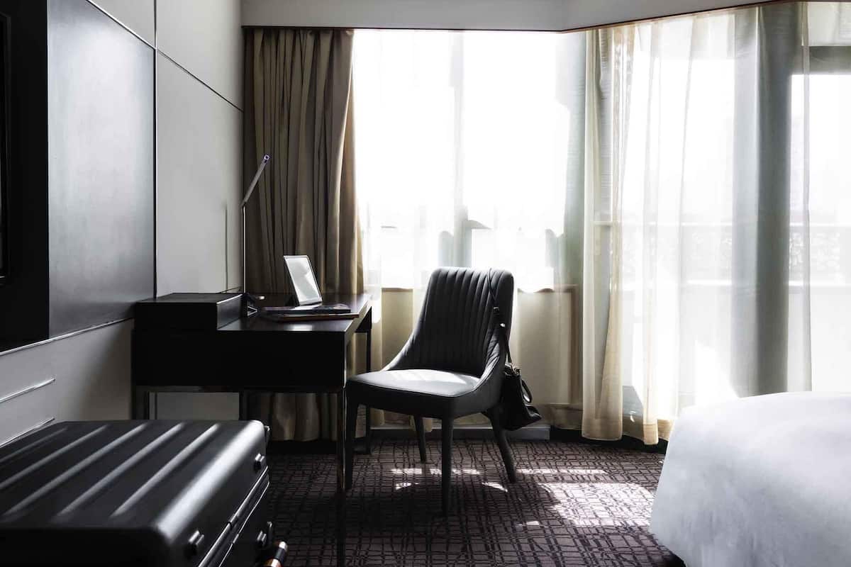 Een hotelkamer met een bed, een bureau met een laptop, een stoel en een koffer.