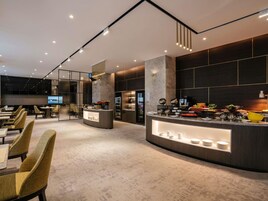 A modern hotel lobby with a central counter, seating area, and a large TV screen.