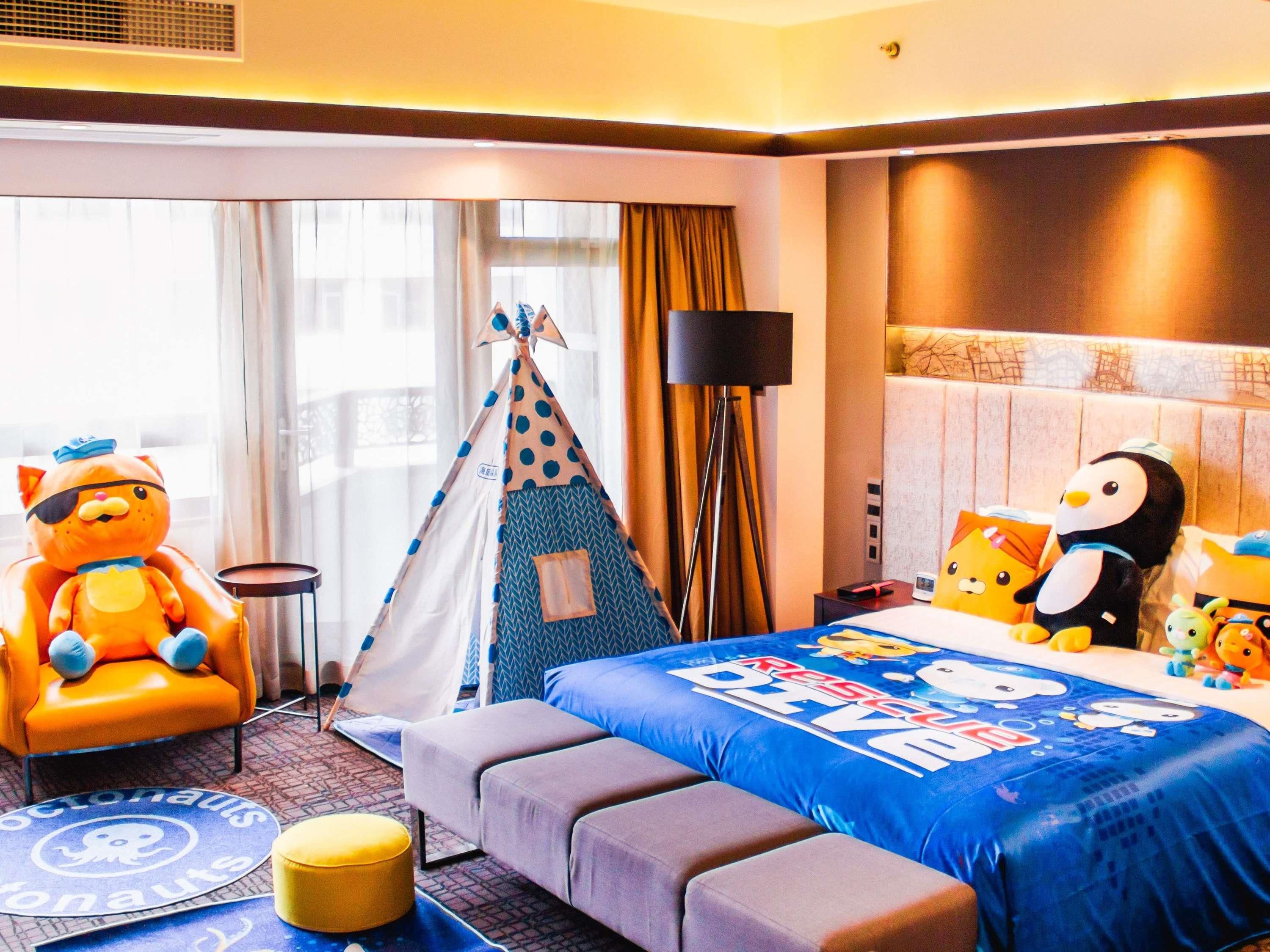 Una habitación de hotel con una cama, un sofá, una silla, una tienda de campaña y juguetes de peluche.