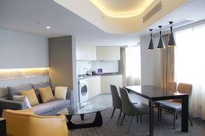 Ein modernes Hotelzimmer mit einer Couch, einem Glastisch, Stühlen, einer Waschmaschine und einer Küchenzeile.