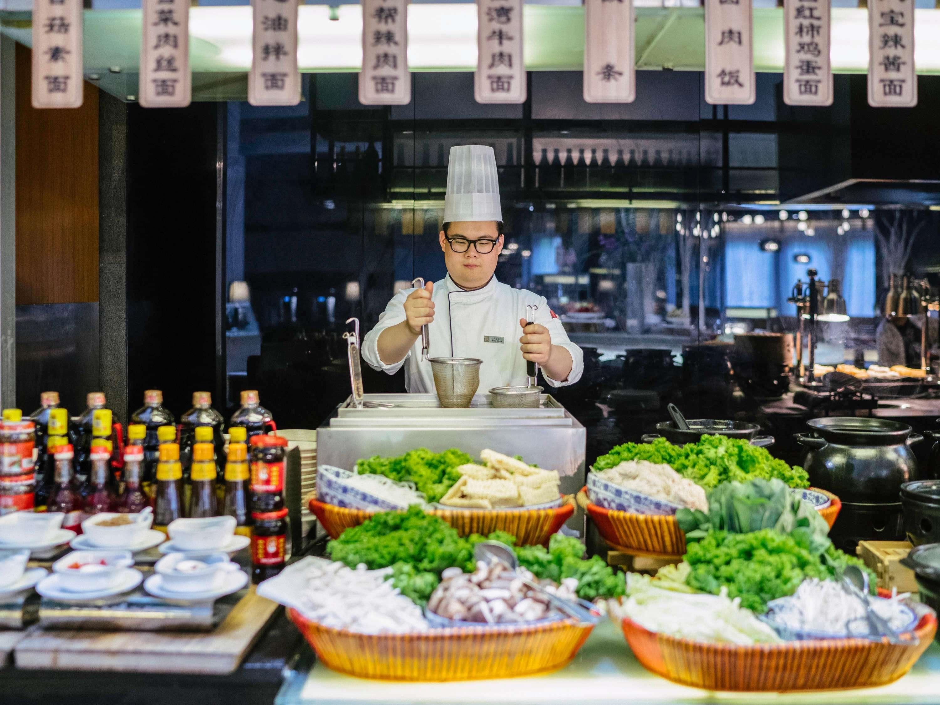 Un chef dans une cuisine professionnelle, avec divers aliments et condiments disposés devant lui.