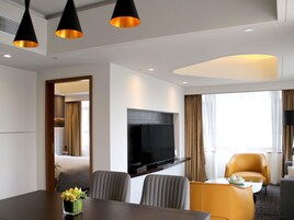 A modern hotel room with a flat-screen TV, a dining table, two chairs, a sofa, and a small table with a teapot.