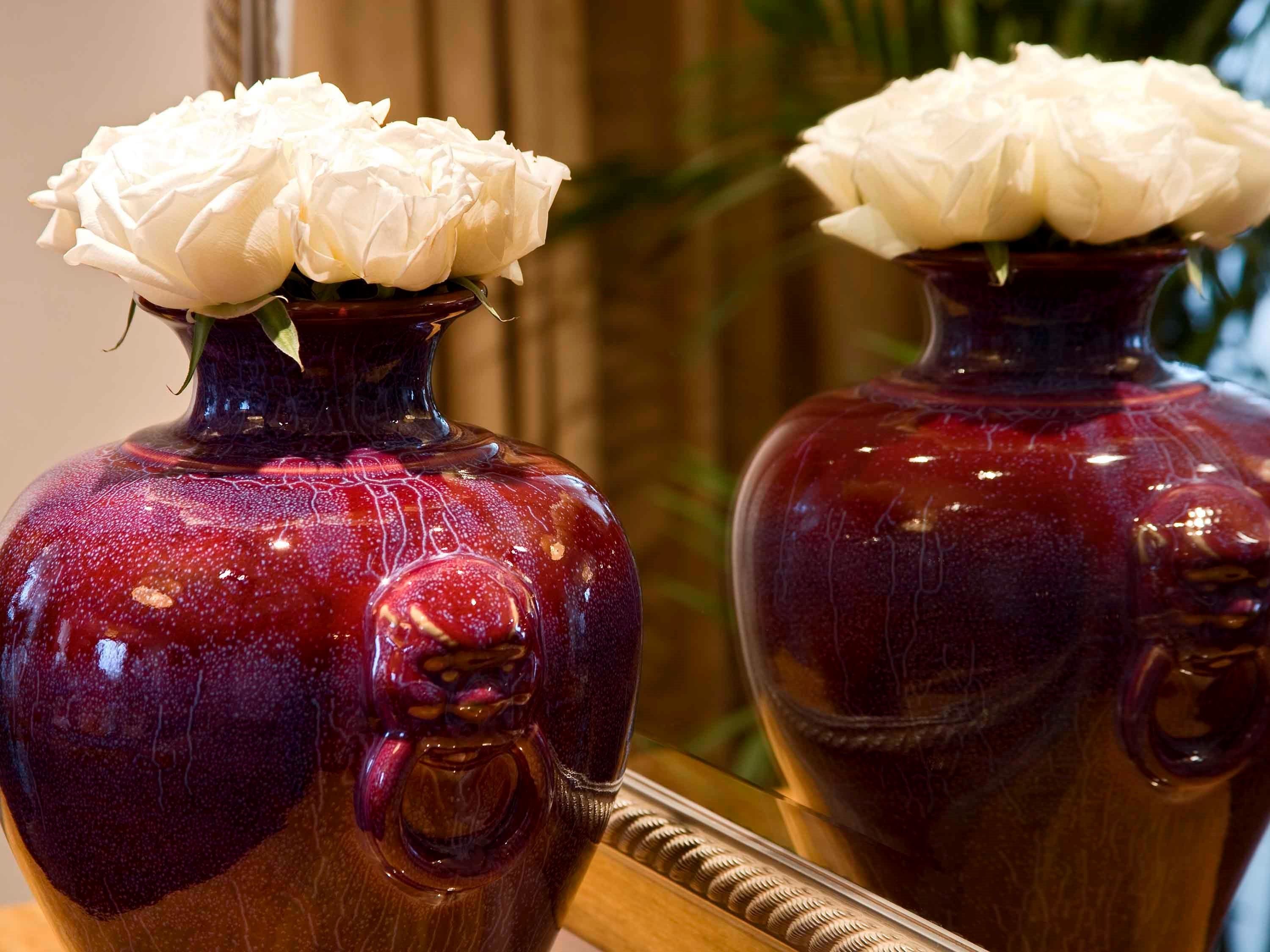 Dos jarrones rojos con flores blancas y un espejo que refleja el jarrón.