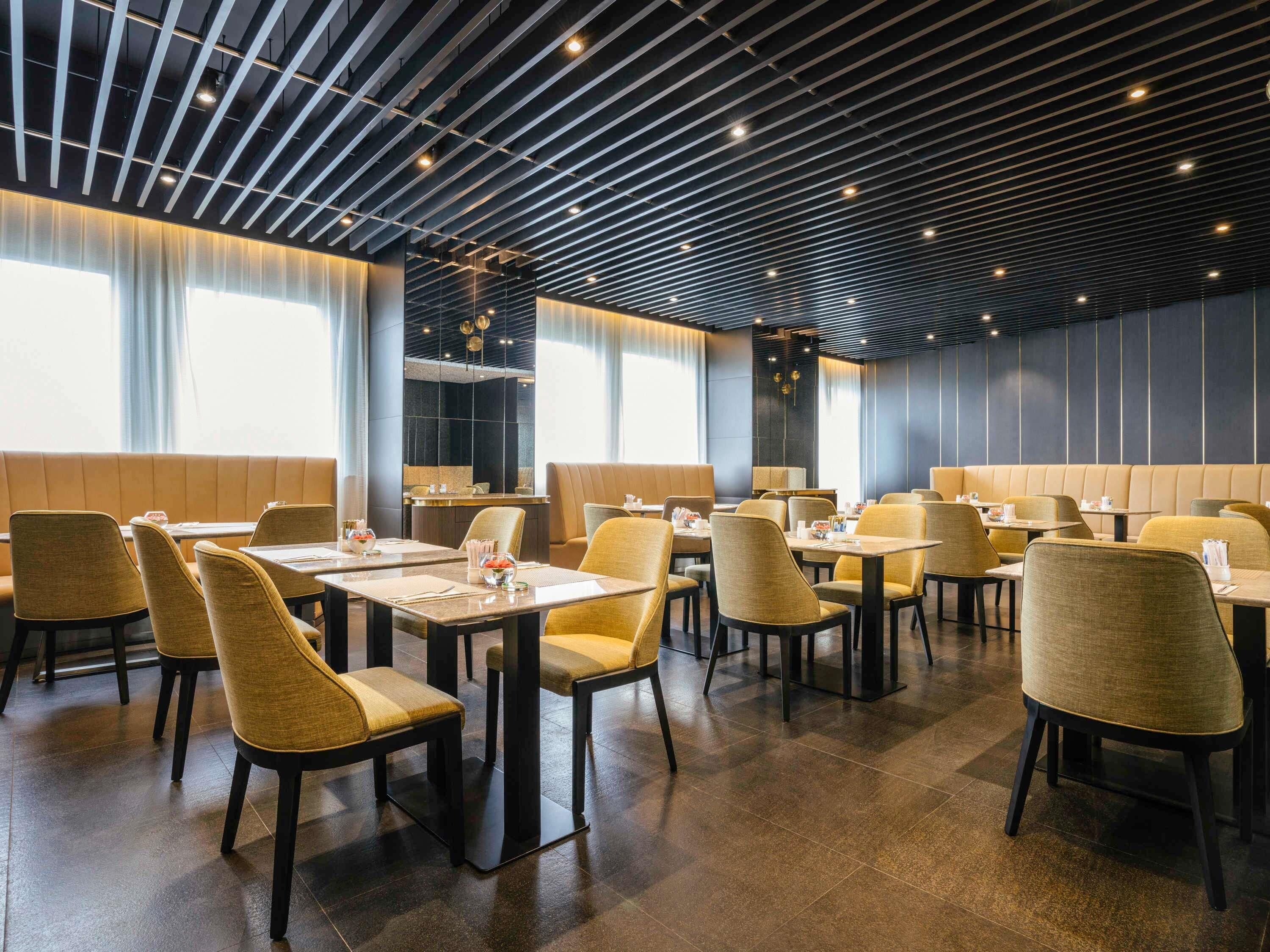 A modern restaurant with booths and tables, featuring a dark ceiling with linear lighting and large windows.