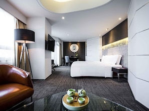 Une chambre d’hôtel moderne équipée d’un lit, d’un bureau, d’une chaise, d’un canapé et d’une table basse avec des tasses.