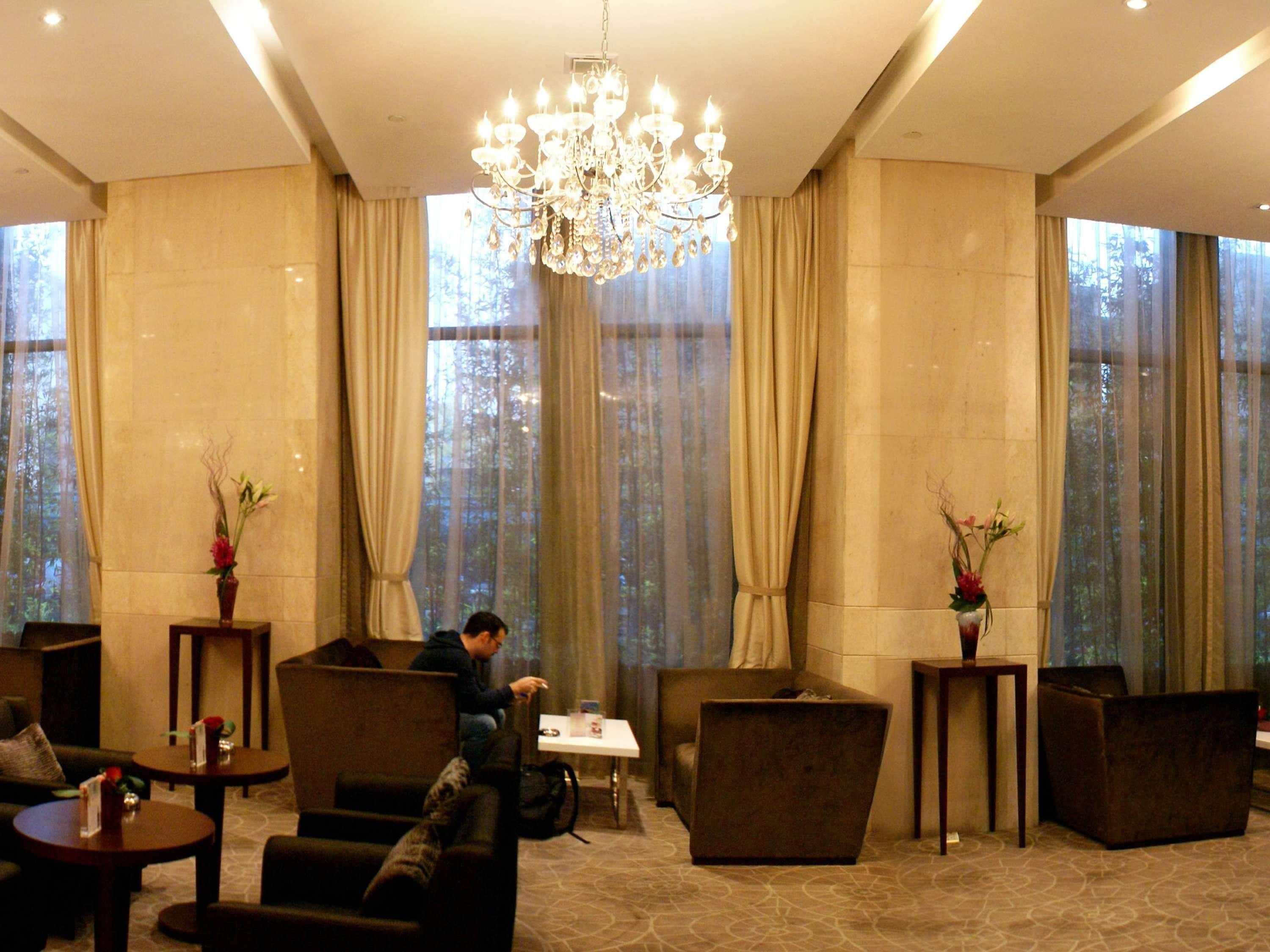 A spacious lobby with a chandelier, comfortable seating, and large windows with curtains.