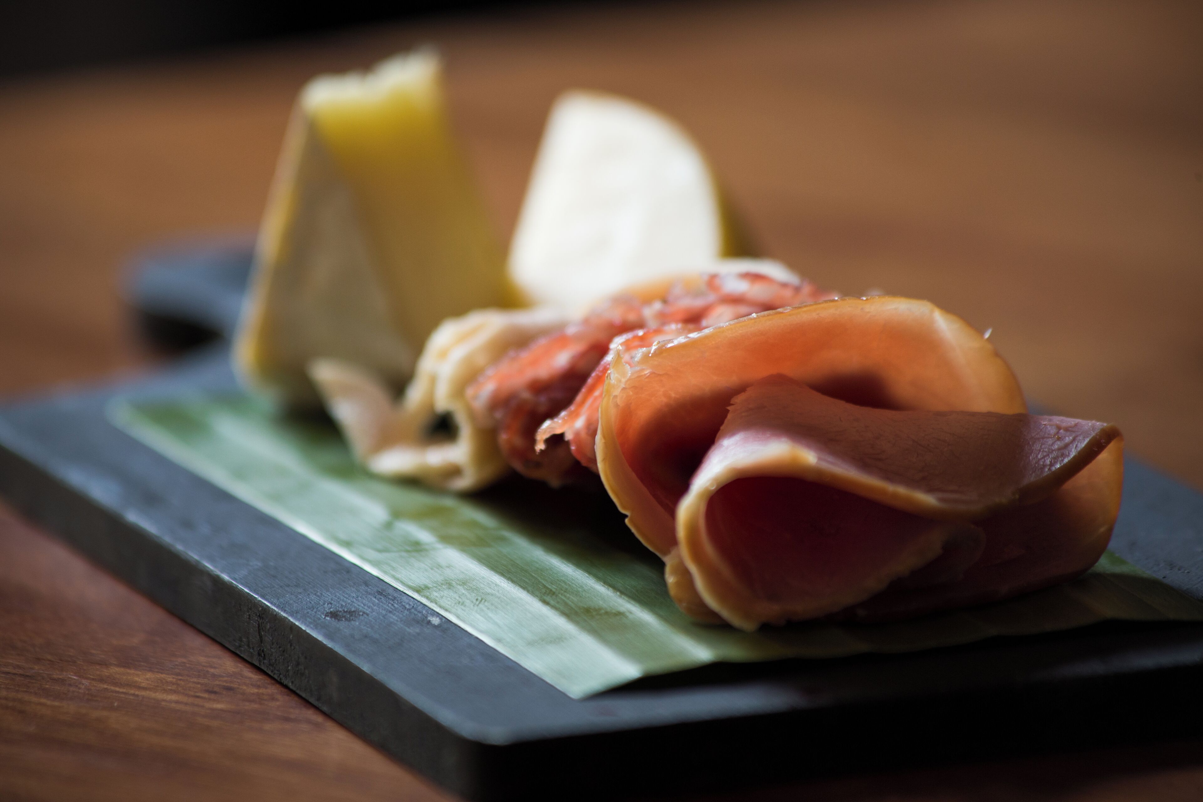 A plate with slices of cured meat and a wedge of cheese on a dark slate plate.