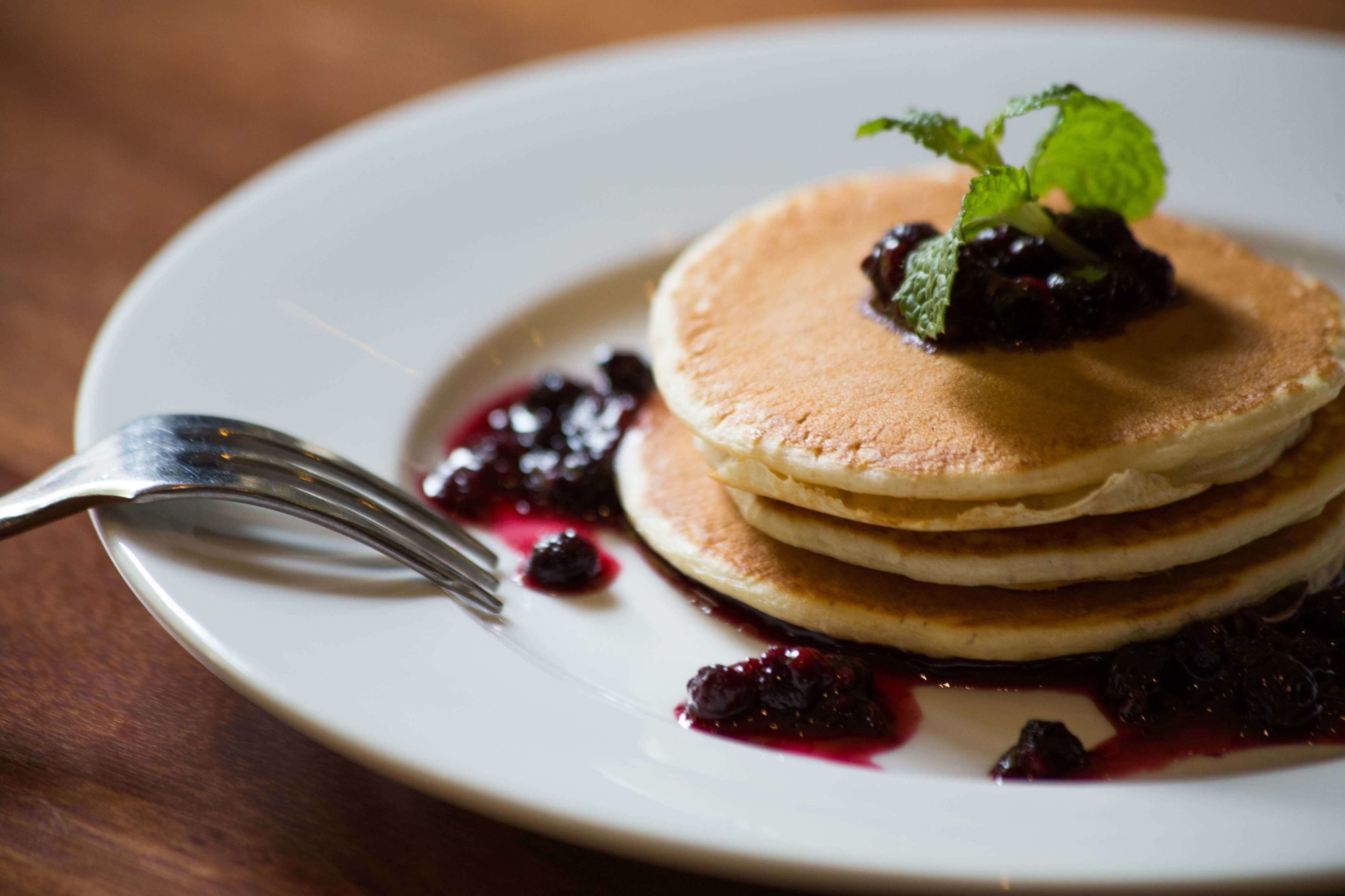A stack of pancakes with berry compote and a mint leaf on a white plate.