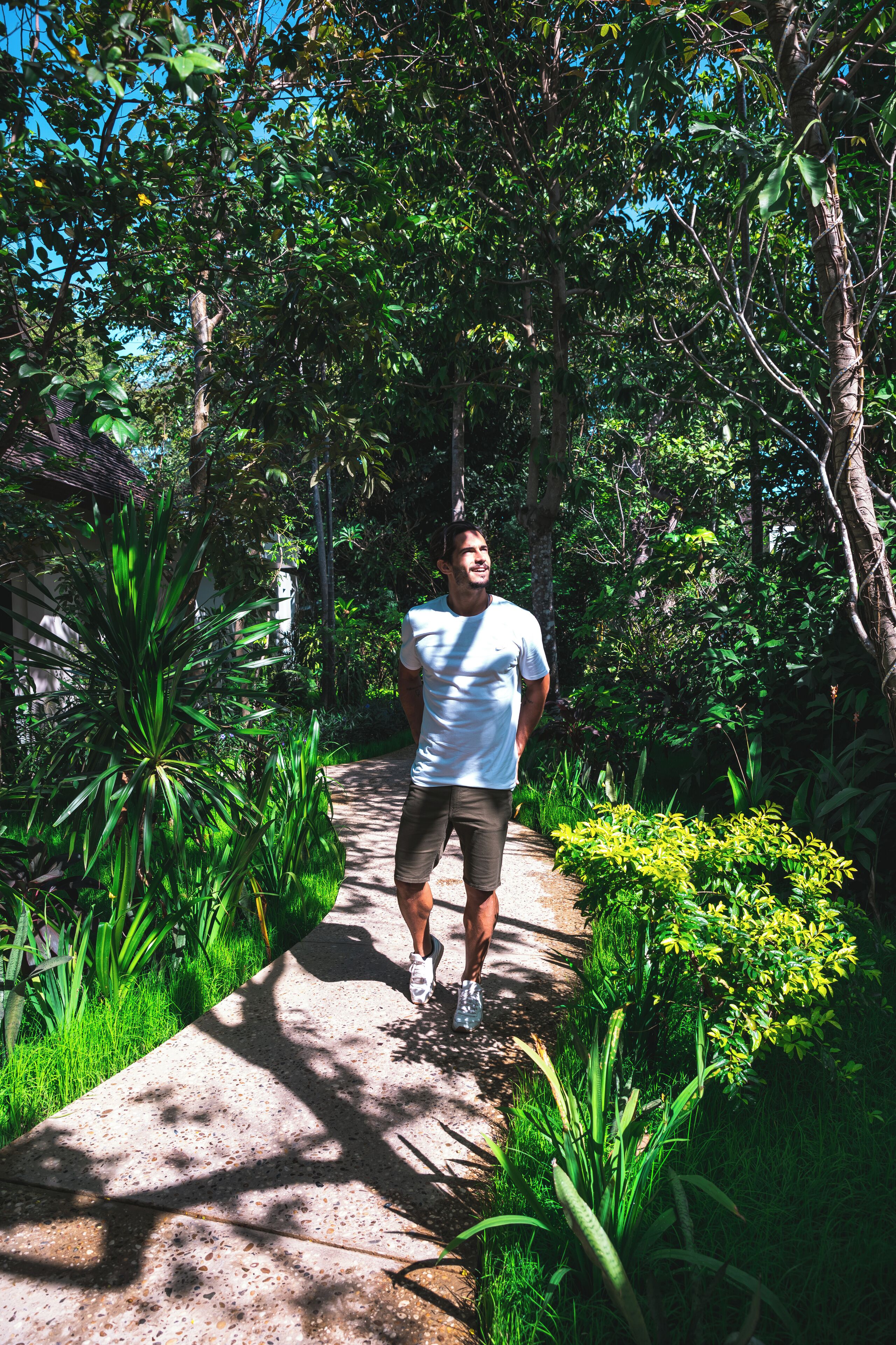 A man walking on a concrete path surrounded by lush greenery and trees.