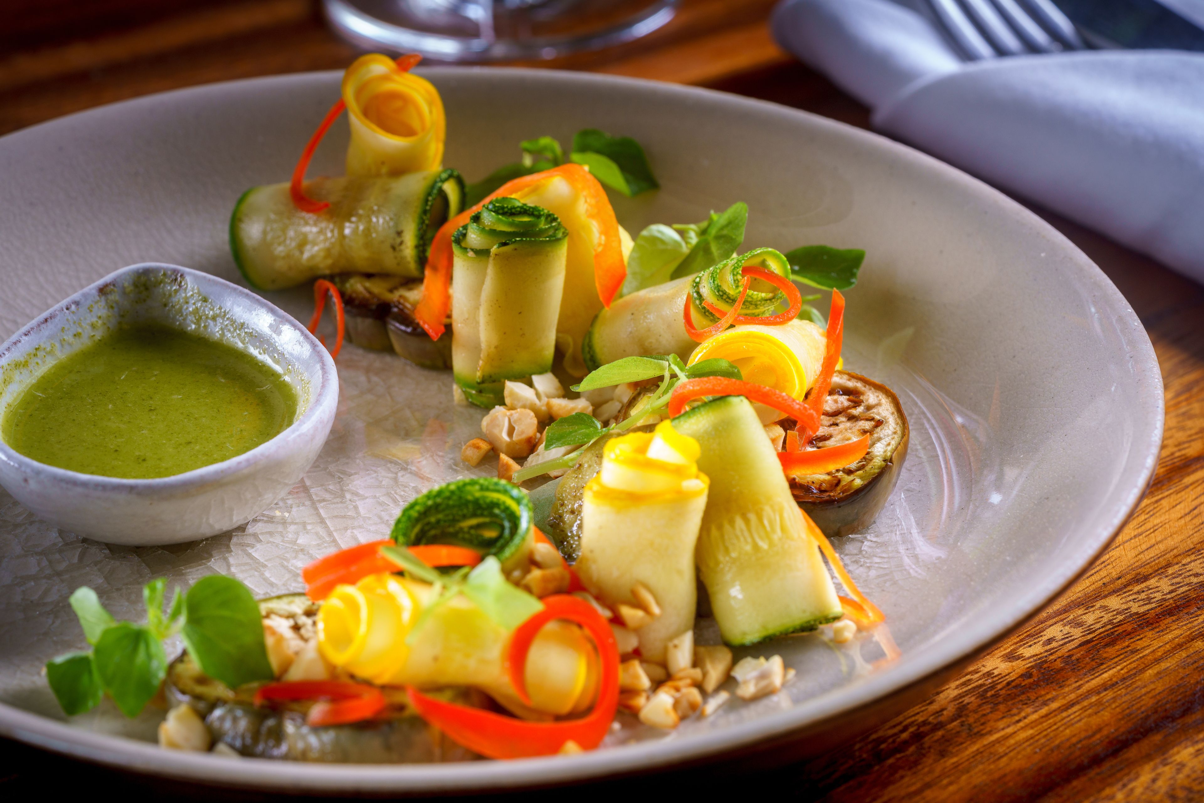 A plate of food with various vegetables and a small bowl of green sauce.