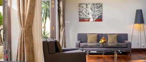 A modern living room with a grey sofa, a glass coffee table, and a painting of a tree on the wall.