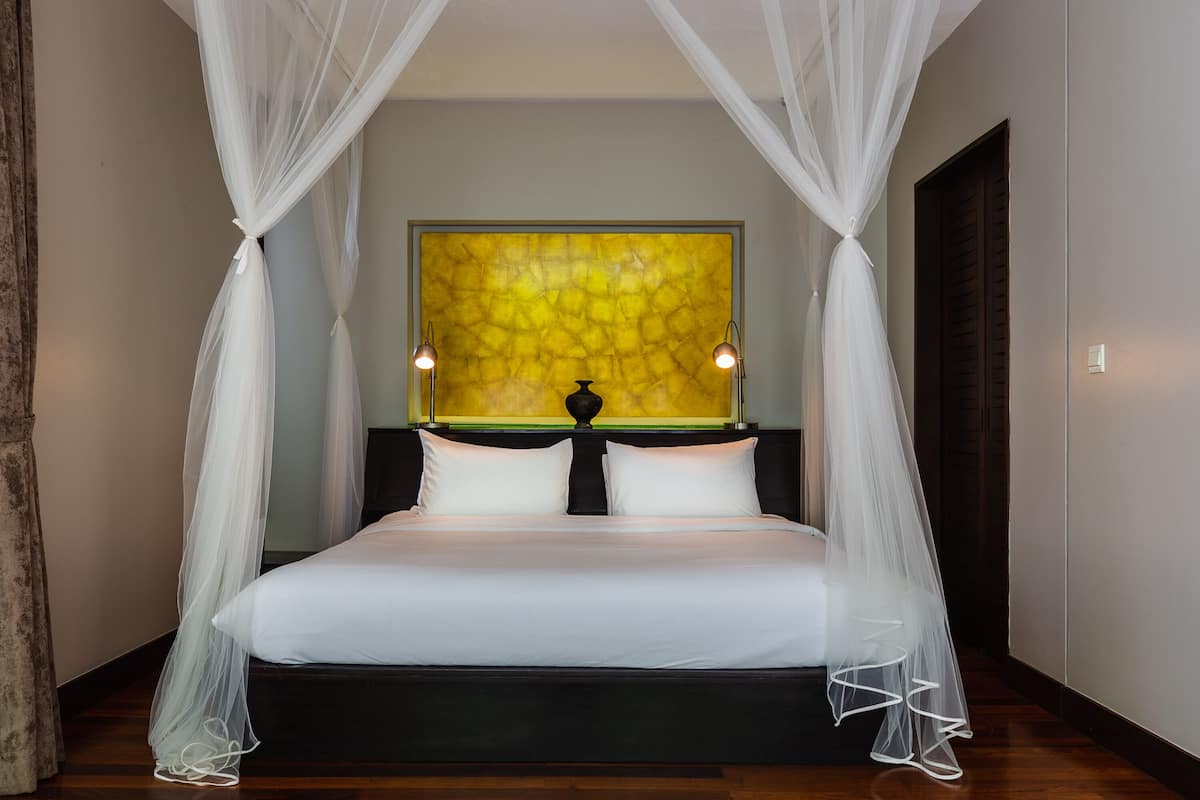 Een bed met witte lakens, een hemelbed en een decoratief kunstwerk erboven.