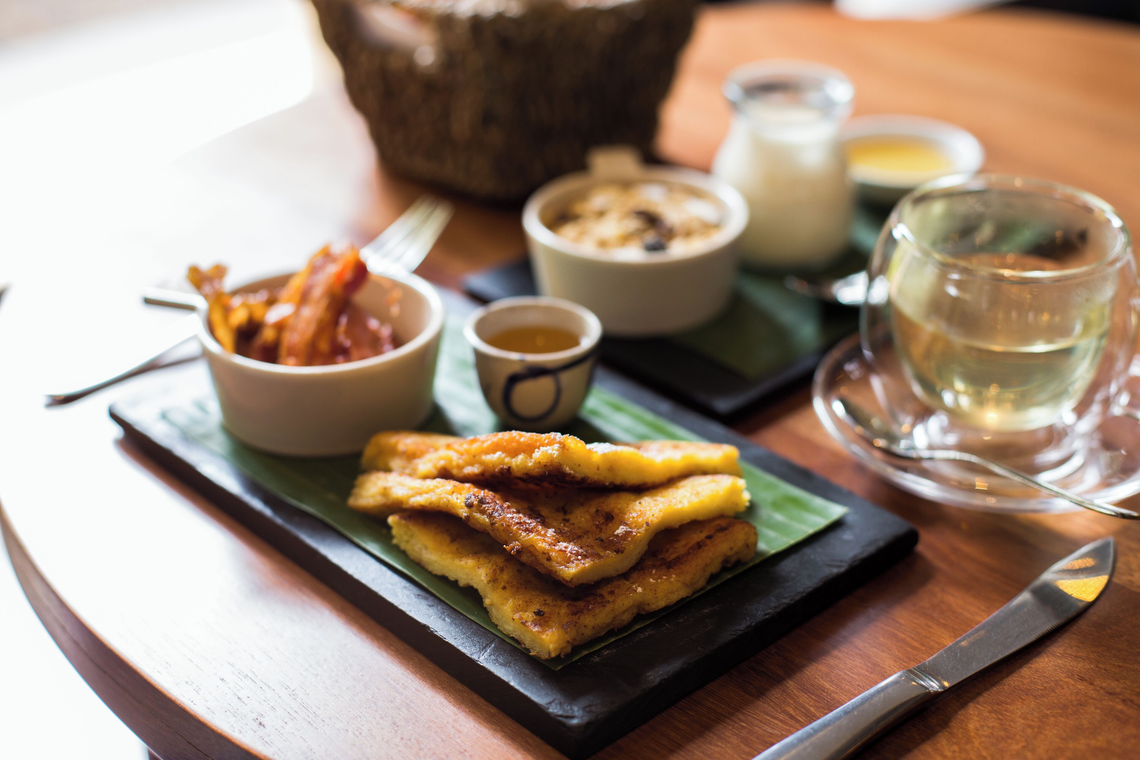 Un repas composé de plats frits, un verre d’eau et de petits bols de sauces, le tout servi sur une table en bois.