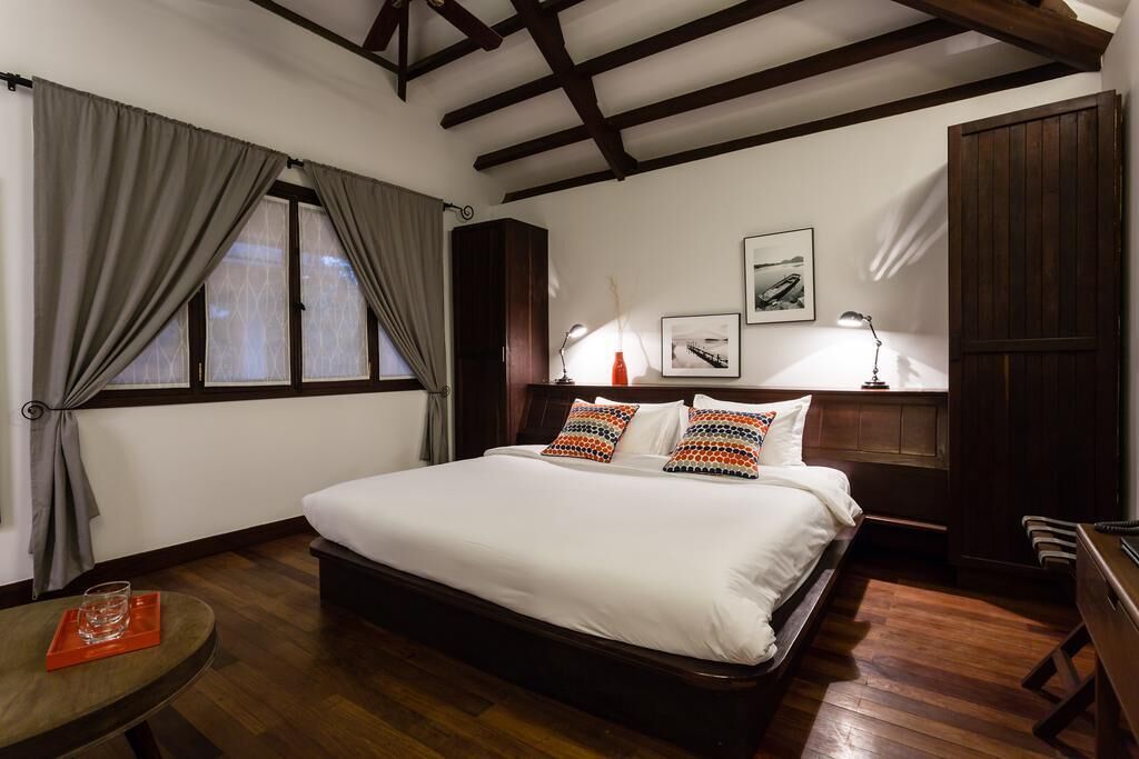 Un dormitorio con una cama grande, suelo de madera, un escritorio y una ventana con cortinas.