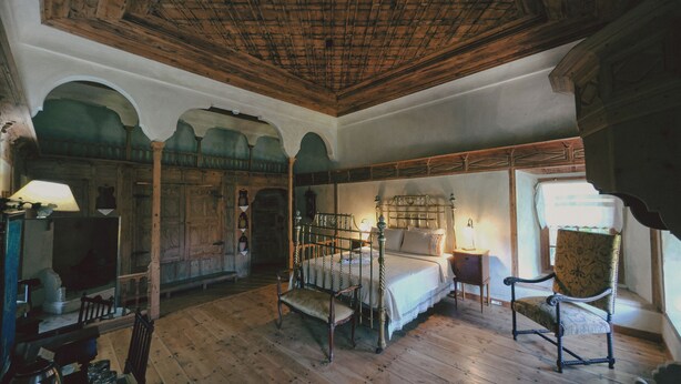 A room with a wooden ceiling, a bed with a metal frame, a wooden chair, and a small table with a lamp. - Heritage Homes Mehmet Ali Aga Konagi (Datça)
