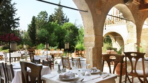 Un área de comedor al aire libre con arcos de piedra, mesas y sillas de madera preparadas para una comida.