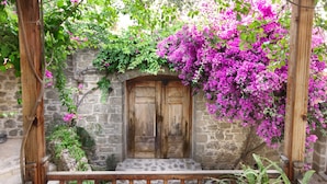 Un edificio de piedra con puerta de madera, rodeado de exuberante follaje y coloridas flores rosadas.