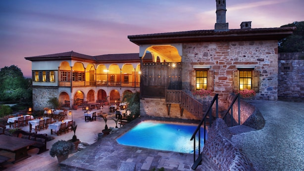 Un patio con piscina, mobiliario exterior y un edificio de piedra con arcos y una escalera.