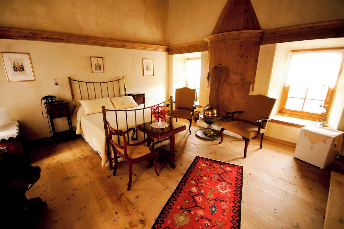 Une chambre traditionnelle avec un lit en bois, une petite table avec une lampe, une chaise et un tapis rouge à motifs.