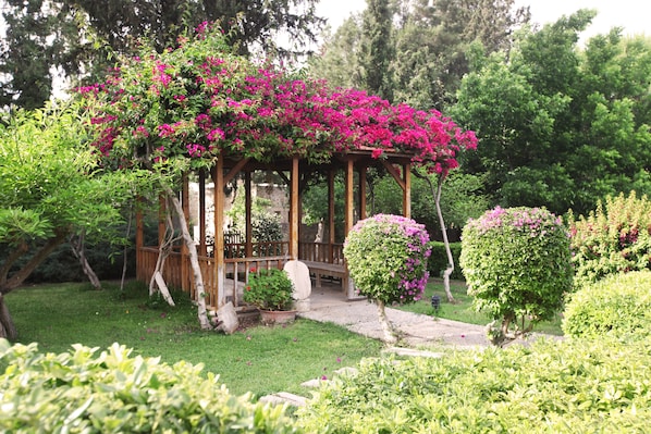 A wooden gazebo with a covered seating area surrounded by lush greenery and flowering plants. - Heritage Homes Mehmet Ali Aga Konagi (Datça)
