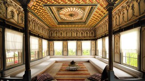 Una habitación con techo alto, diseño ornamental en el techo, ventanas grandes y una alfombra central.