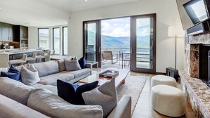 A spacious living room with a large sofa, ottomans, and a coffee table. A fireplace and a television are mounted on the wall. - The Arrabelle, A RockResort, by Vail Resorts (Vail)