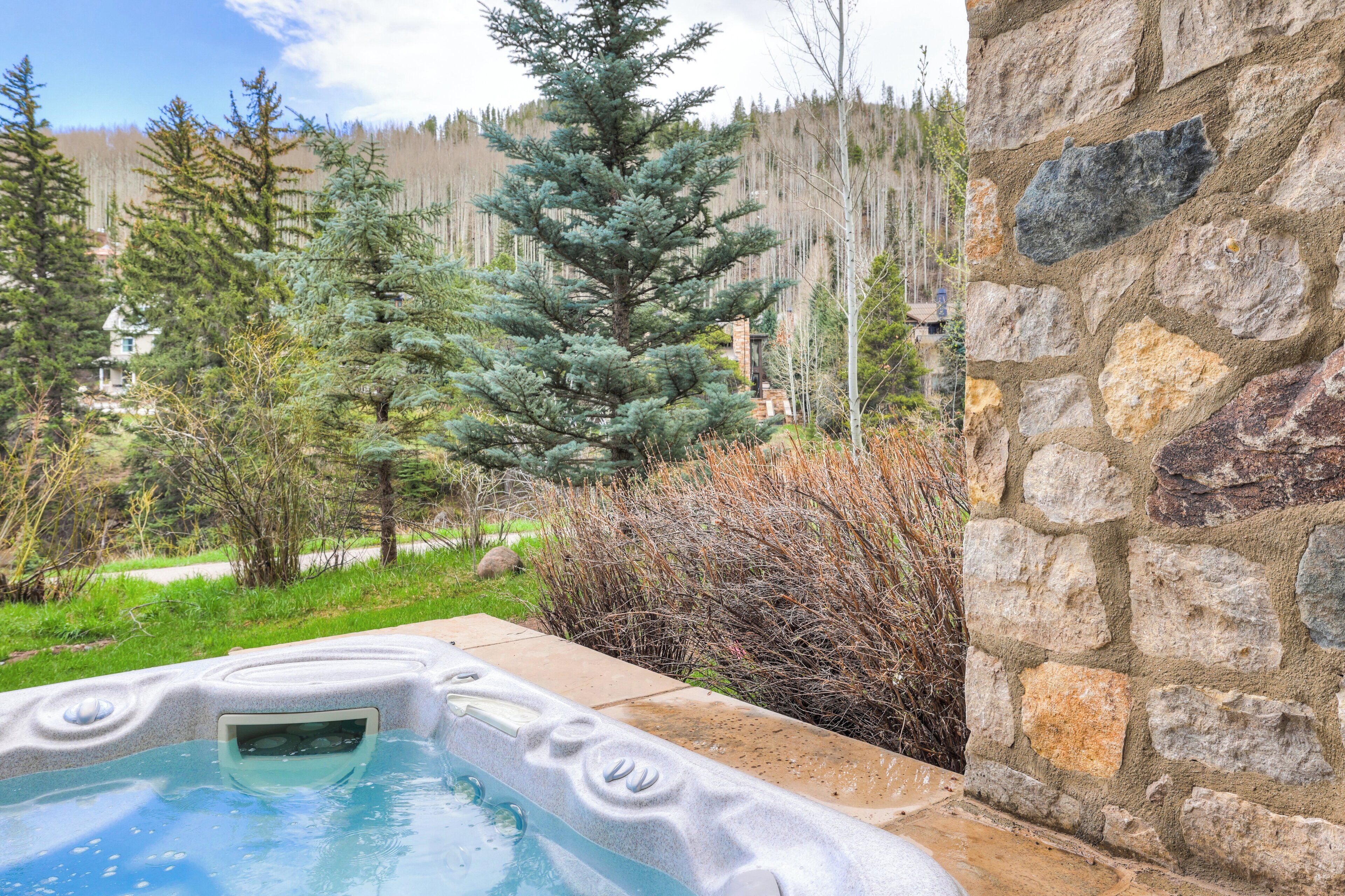 A hot tub with a stone wall and a view of a forested area.