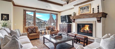 A spacious living room with a fireplace, comfortable seating, and a large window offering a view of a mountain.