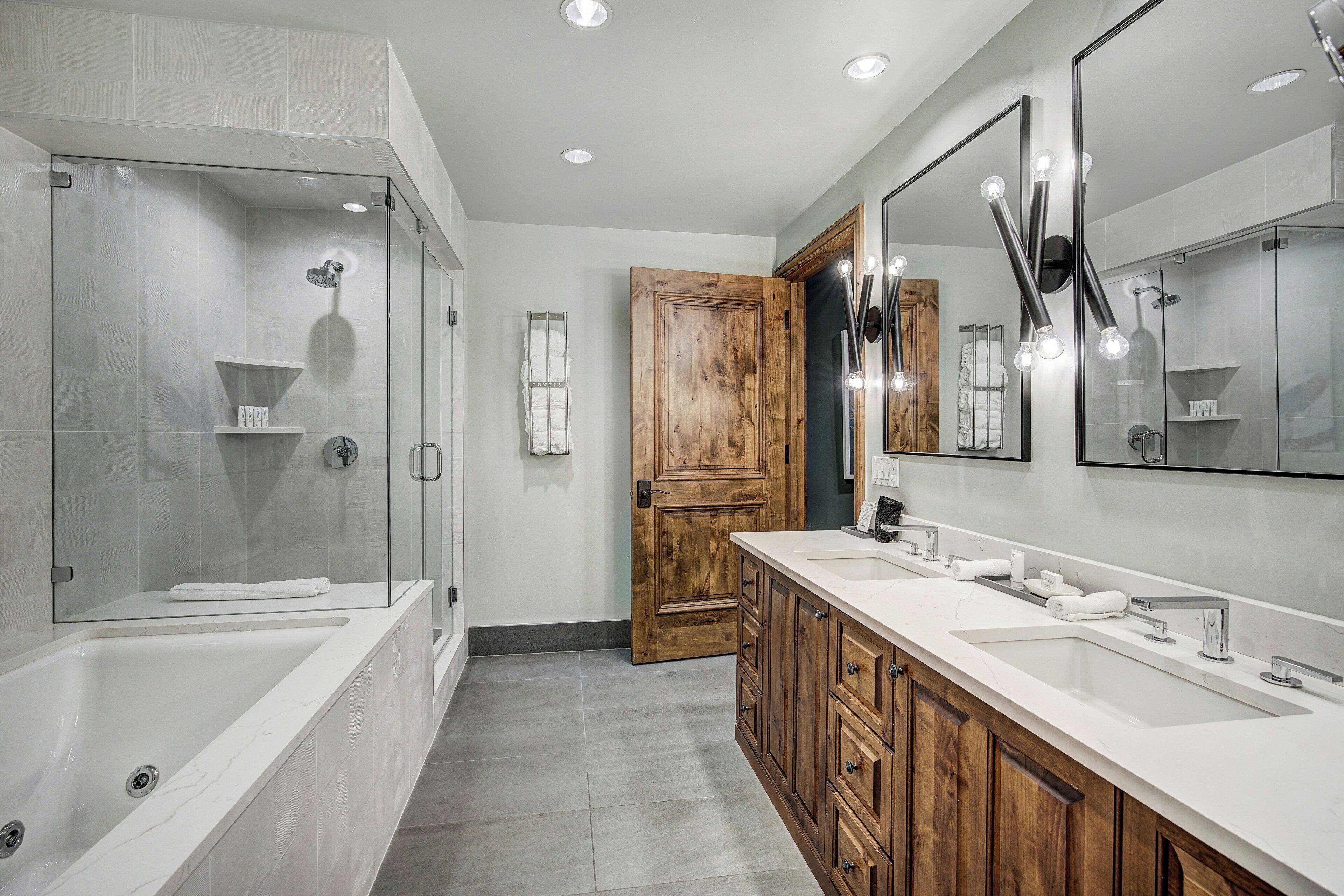 A modern bathroom with a glass-enclosed shower, a wooden door, and a vanity with a large mirror.