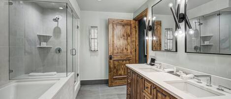 A modern bathroom with a glass-enclosed shower, a wooden door, and a vanity with a large mirror.
