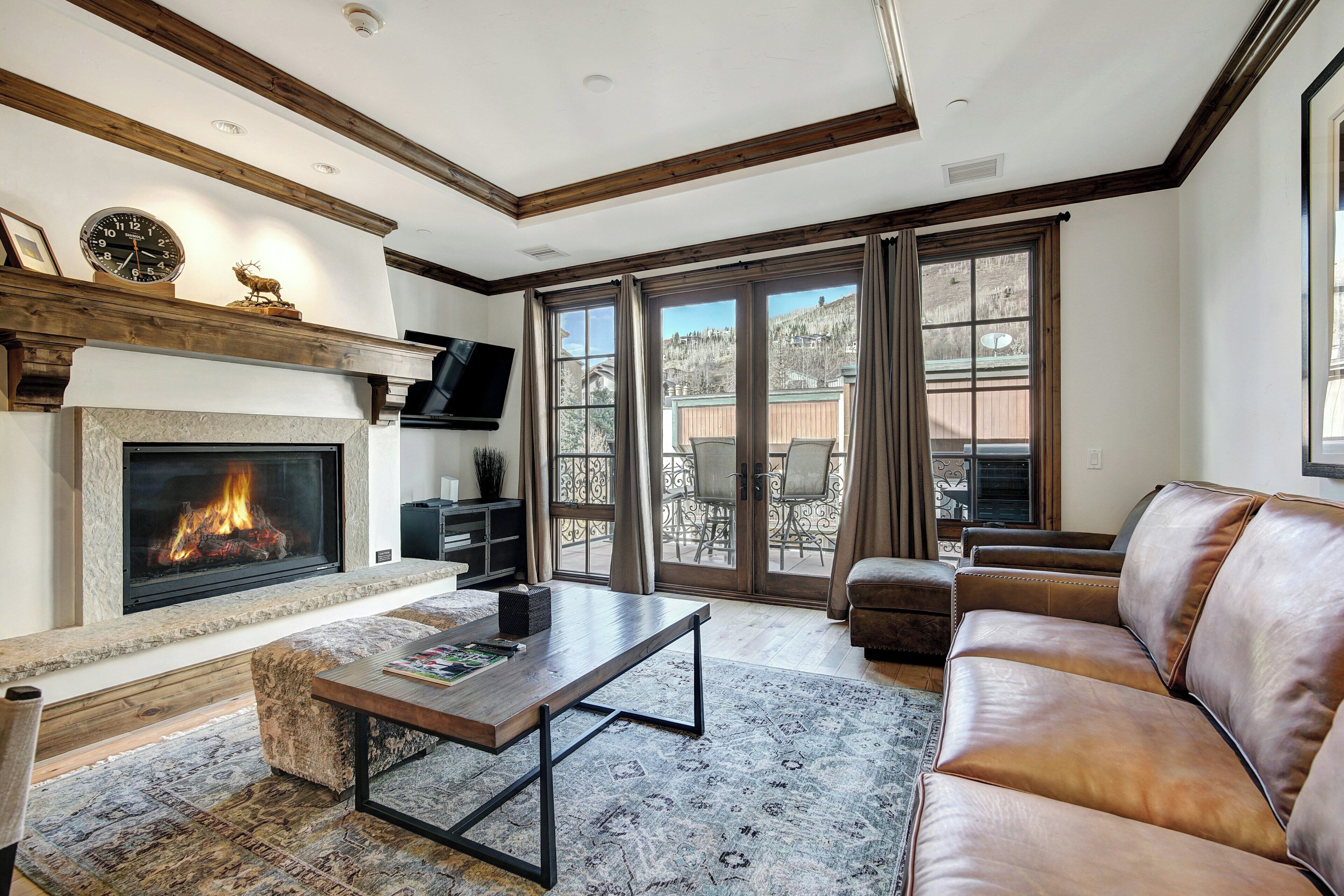 A living room with a fireplace, a sofa, a coffee table, and a large window with a view of a mountain.