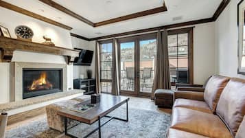 A living room with a fireplace, a sofa, a coffee table, and a large window with a view of a mountain.