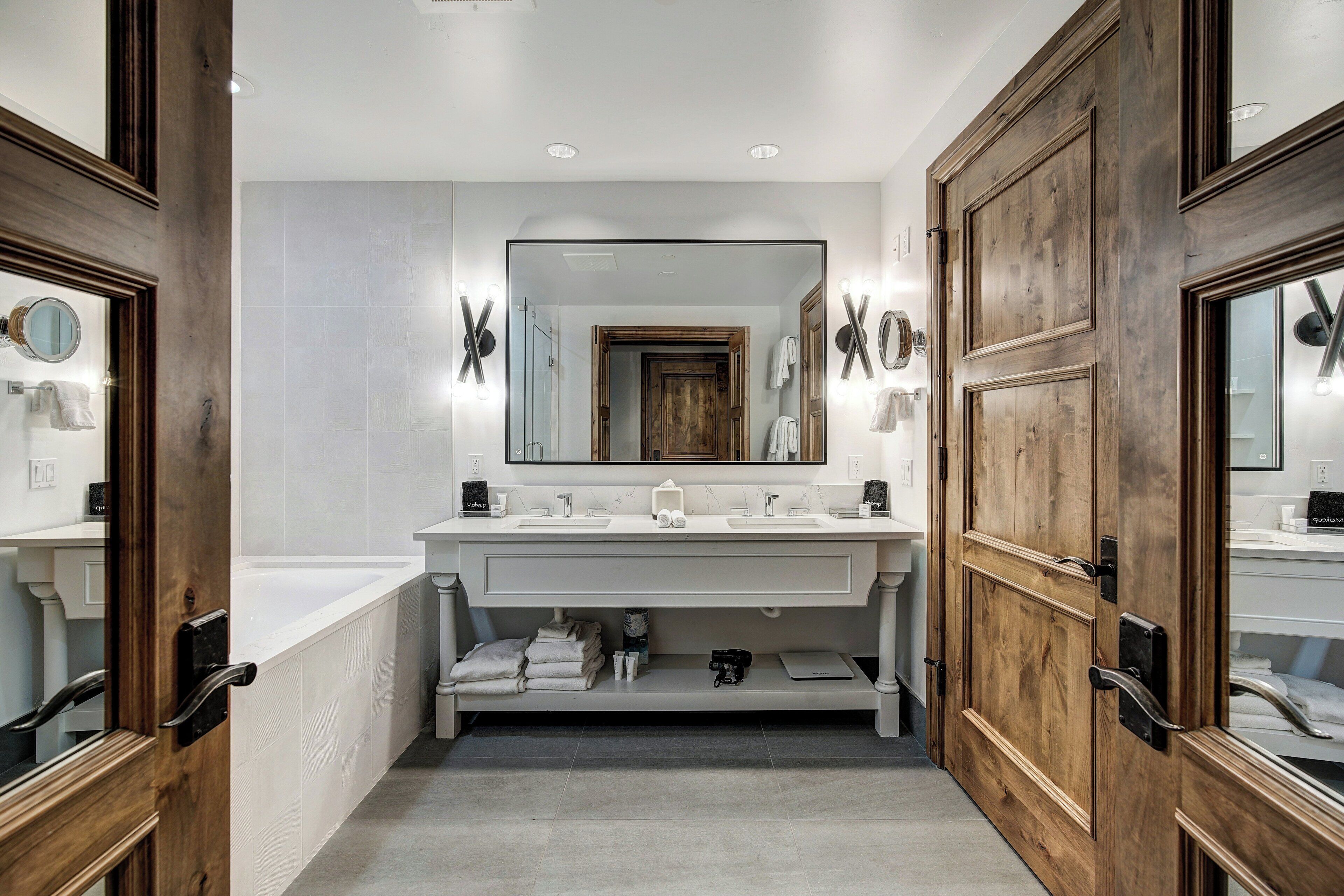 A modern bathroom with a large mirror, two sinks, and a wooden vanity.