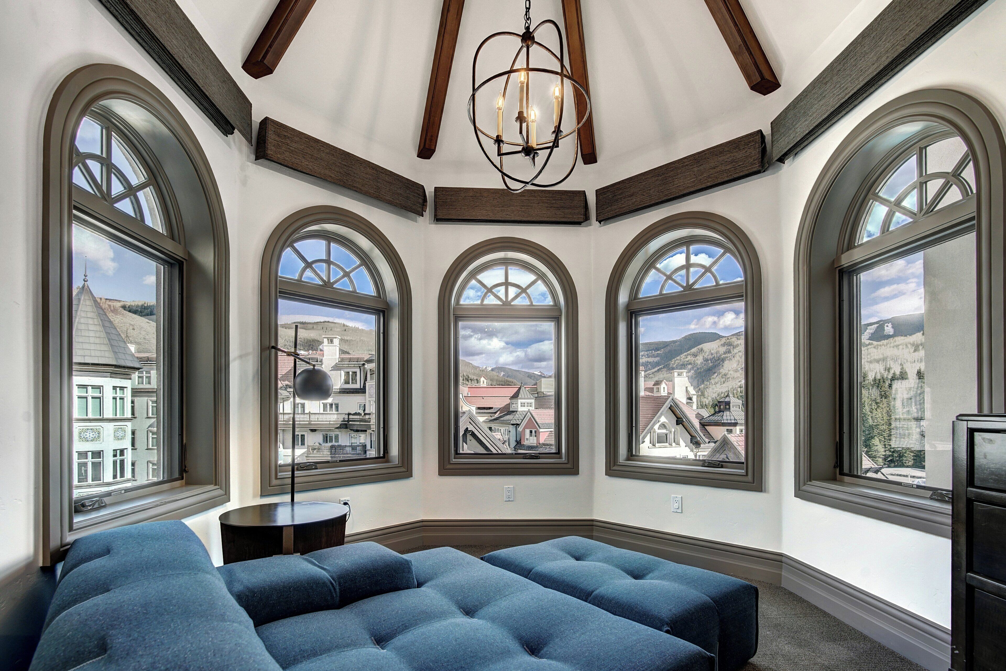 A room with large arched windows, a chandelier, and a tufted blue sofa.