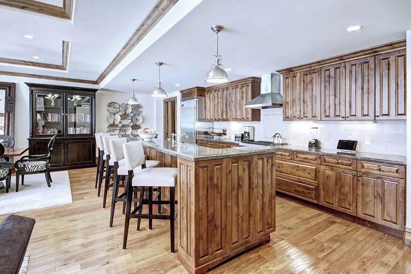 Une cuisine spacieuse avec des meubles en bois, un grand îlot central, des tabourets de bar et des luminaires suspendus.
