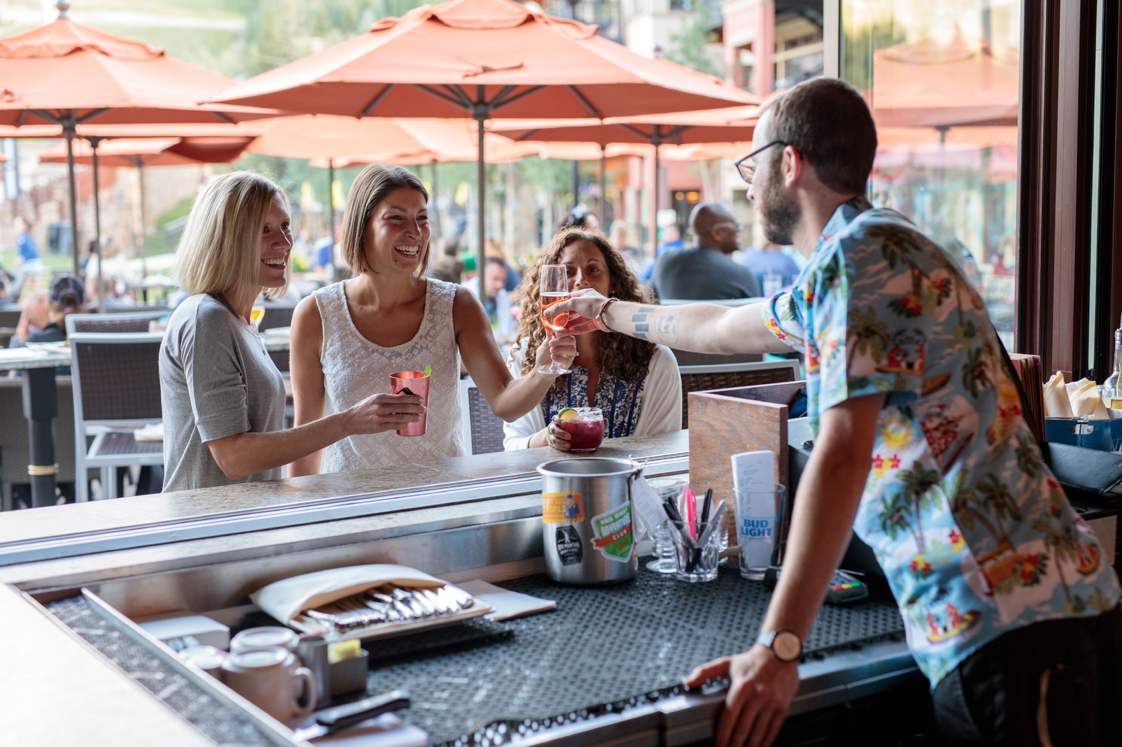 A bar area with a counter, red umbrellas, and a person serving drinks.