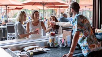 A bar area with a counter, red umbrellas, and a person serving drinks.