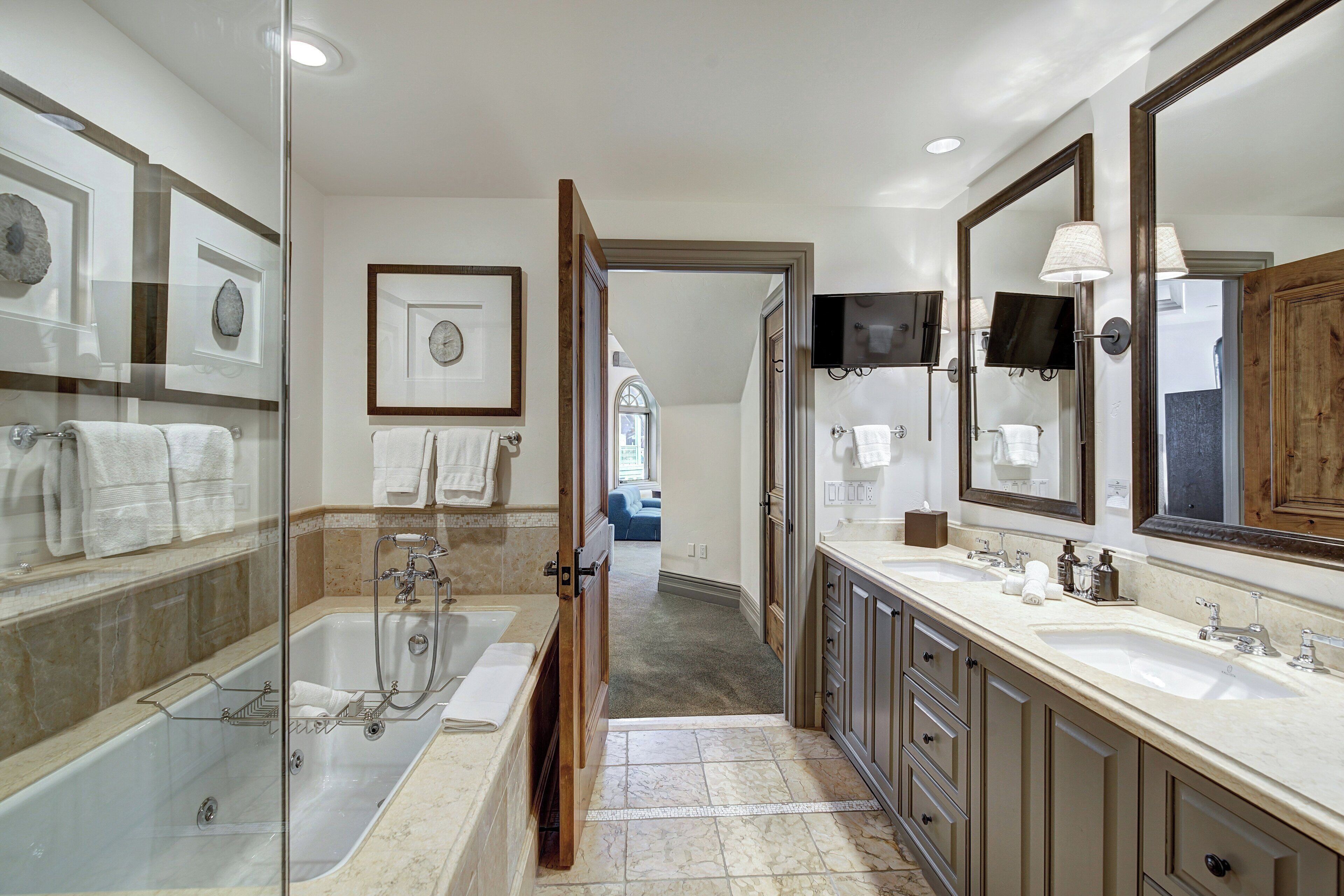 A modern bathroom with a glass-enclosed shower, dual sinks, and a vanity with a large mirror.