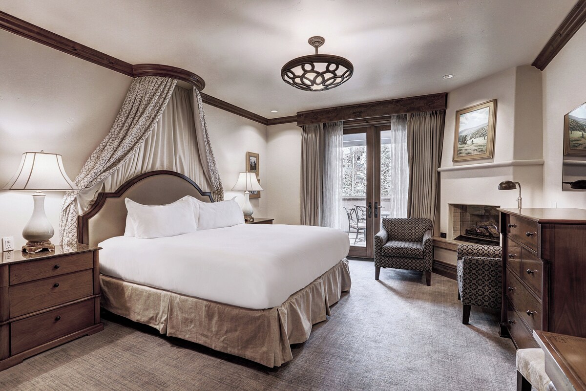 Un grand lit à baldaquin, une chaise, une commode et une cheminée.