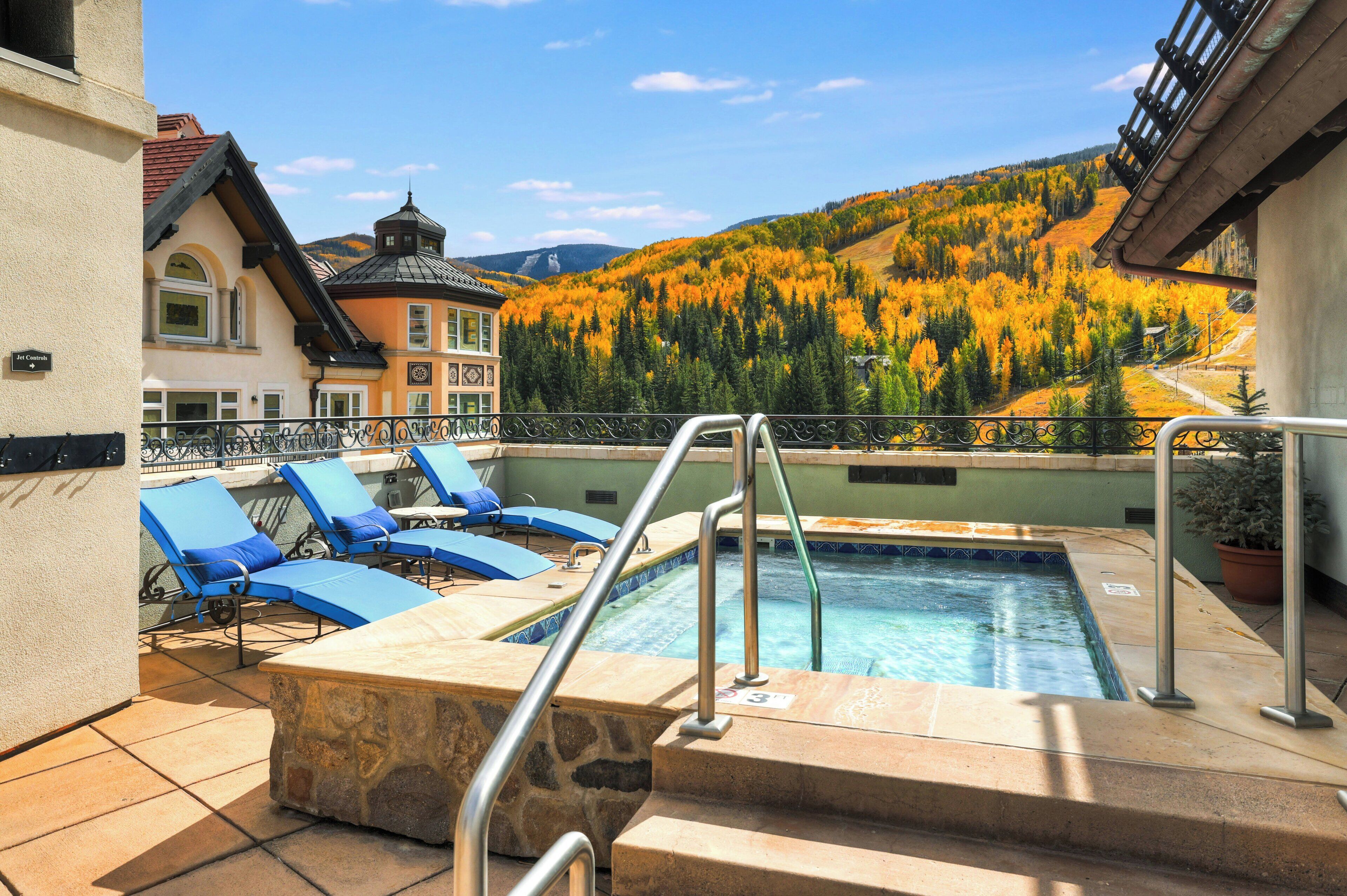 A pool area with lounge chairs and a view of a forested mountain.