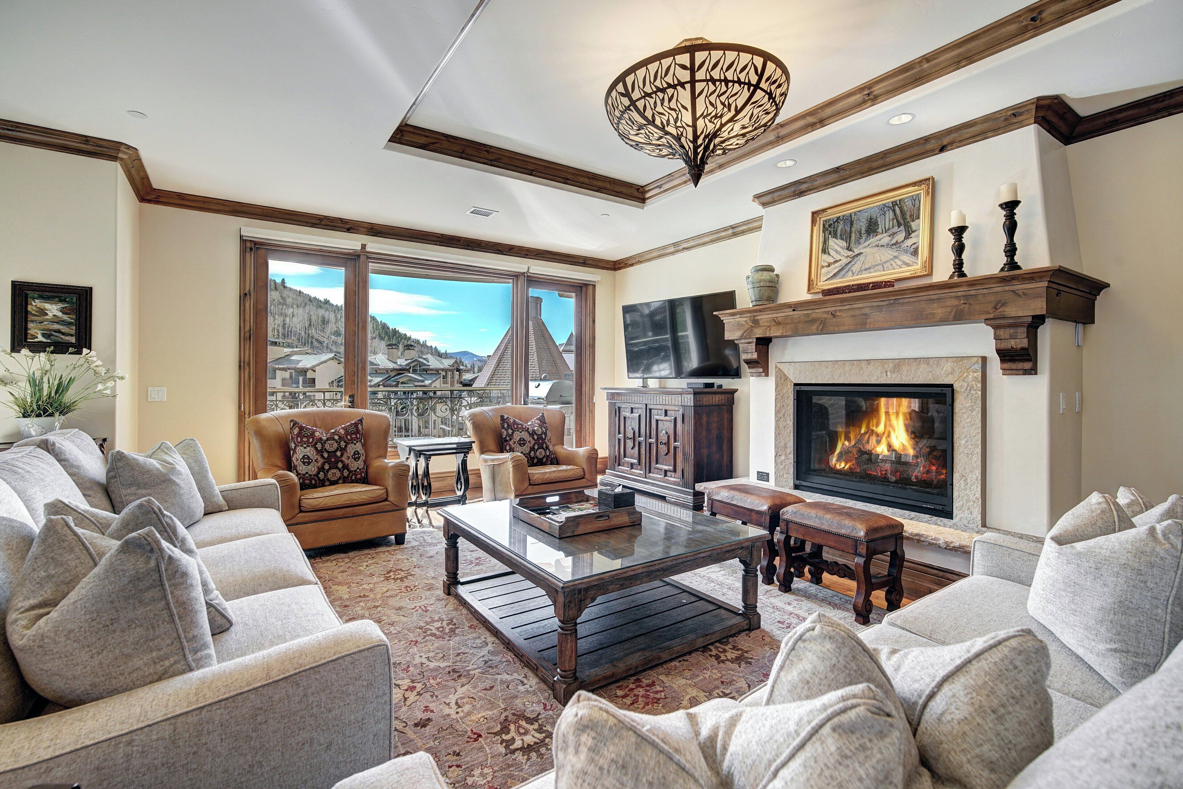 A spacious living room with a fireplace, comfortable seating, and a large window offering a view of the mountains.