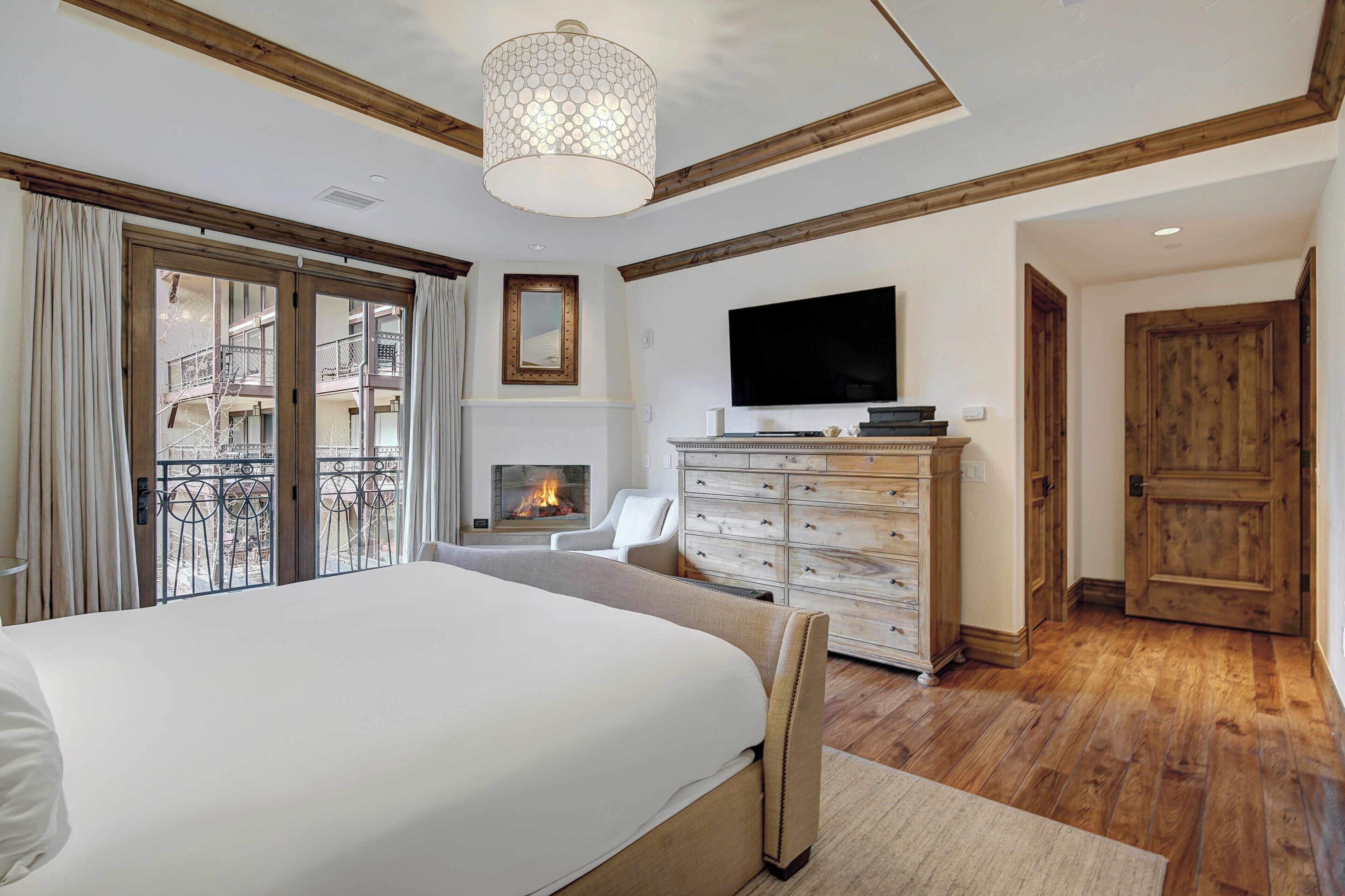A bedroom with a large bed, a fireplace, a television, and a wooden door.